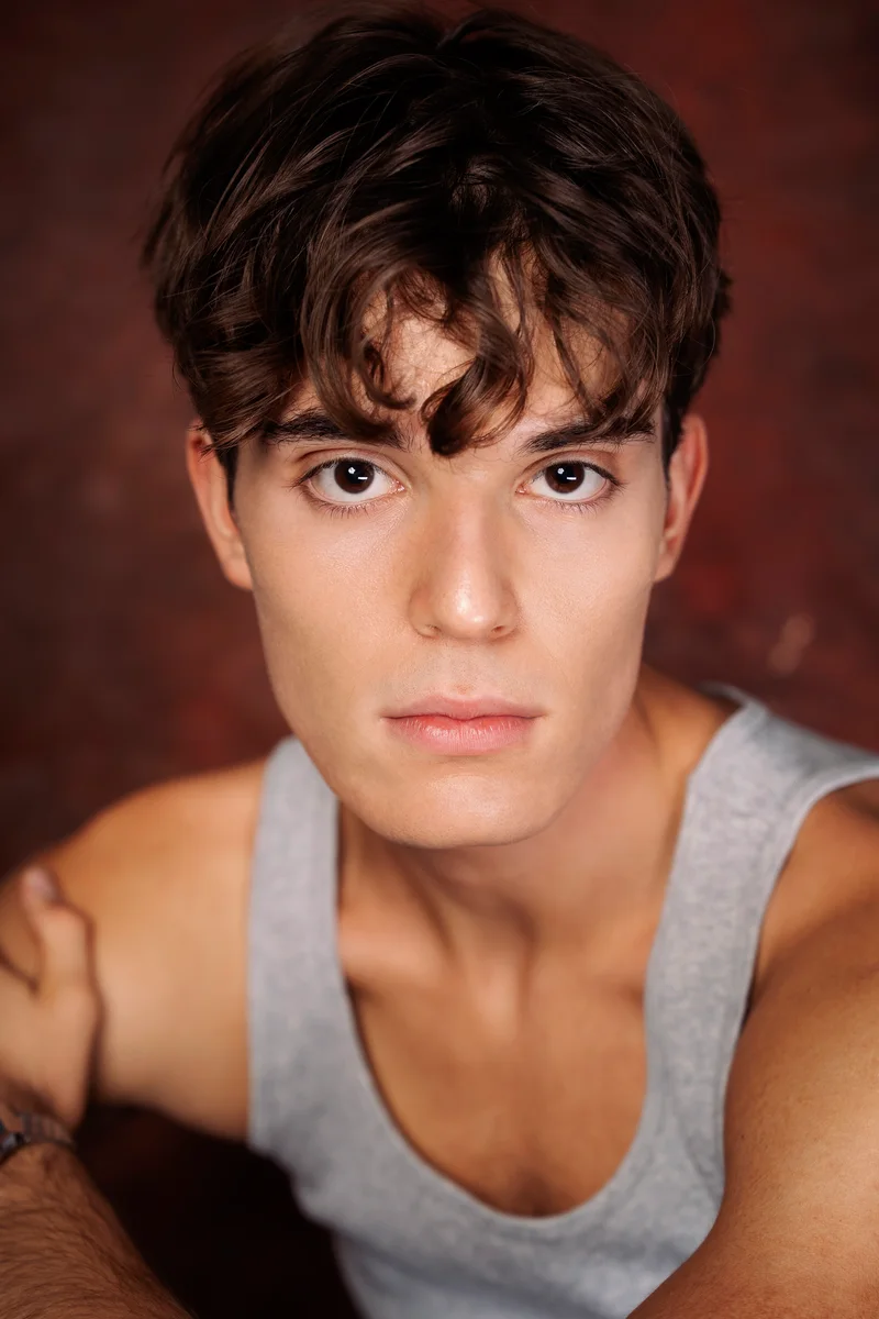 Portrait with short tousled hair and a grey vest against a warm brown backdrop
