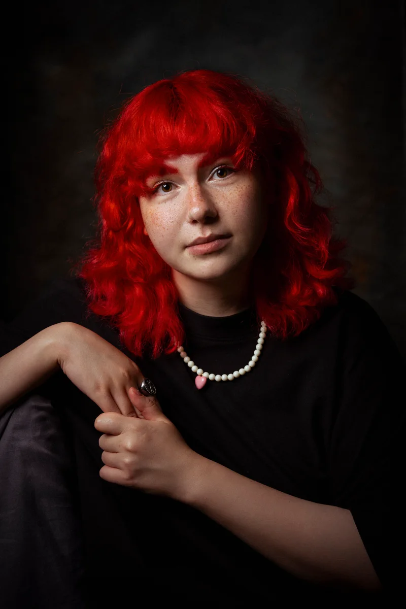 Woman with bright red hair in a black T-shirt, sitting with her arms on her knee