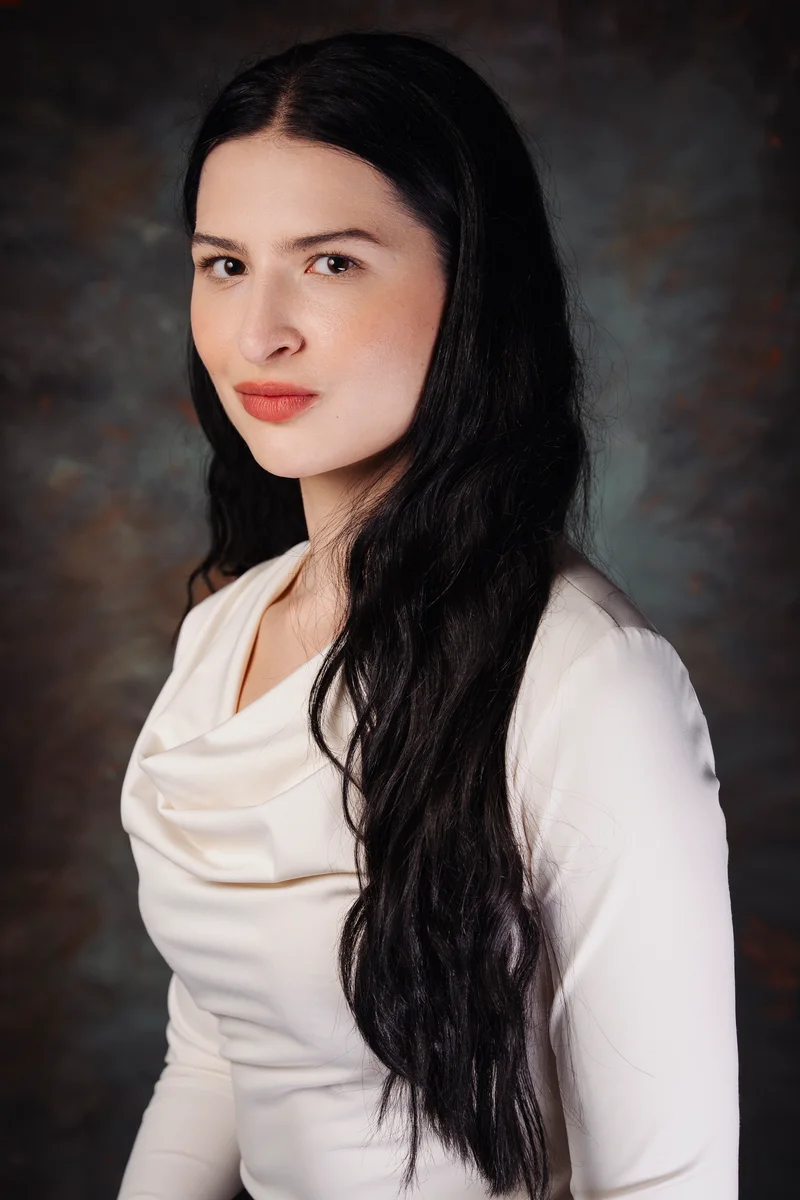 Woman with long black hair in a cream blouse, turned three-quarters