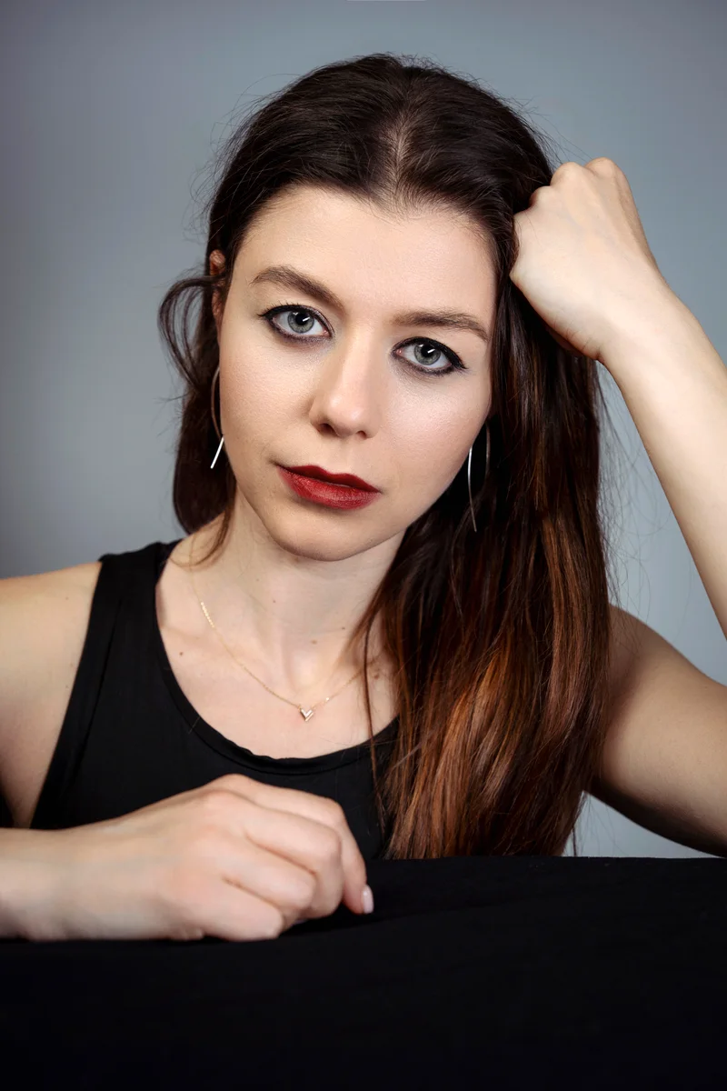 Woman with straight dark hair and a black vest running her hand through her hair