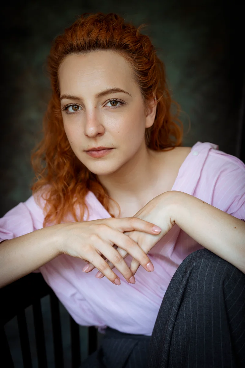 Woman with ginger hair in a pink shirt, sitting with her arms on her knee