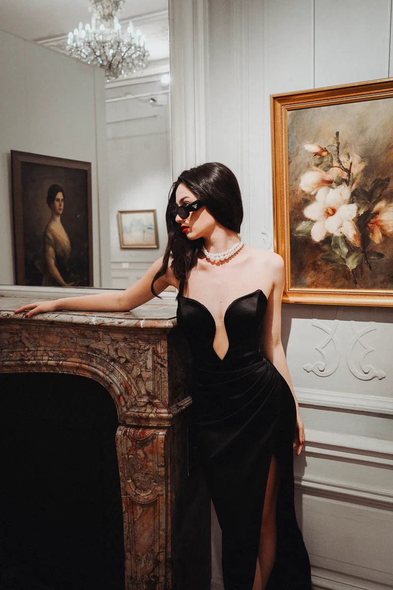 Woman in sunglasses and pearls leaning on a fireplace