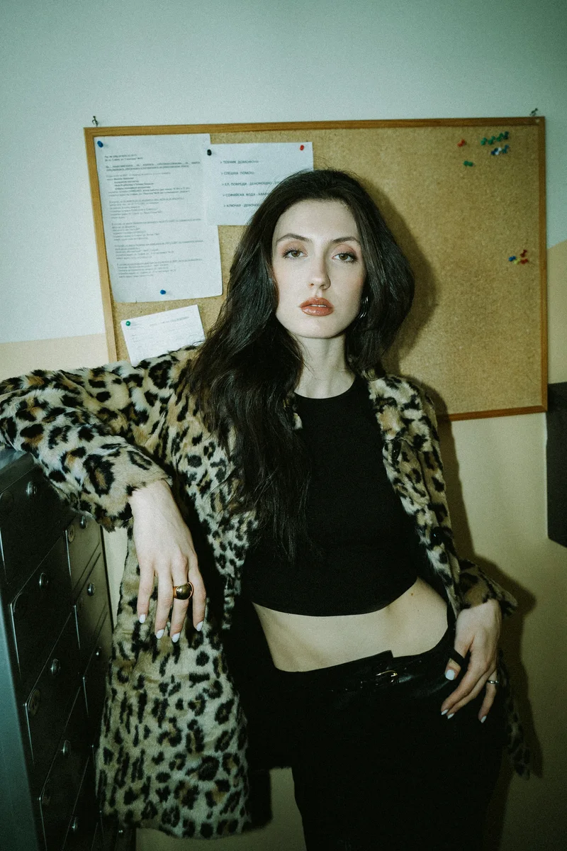 Woman in a leopard-print coat and black top standing beside a noticeboard