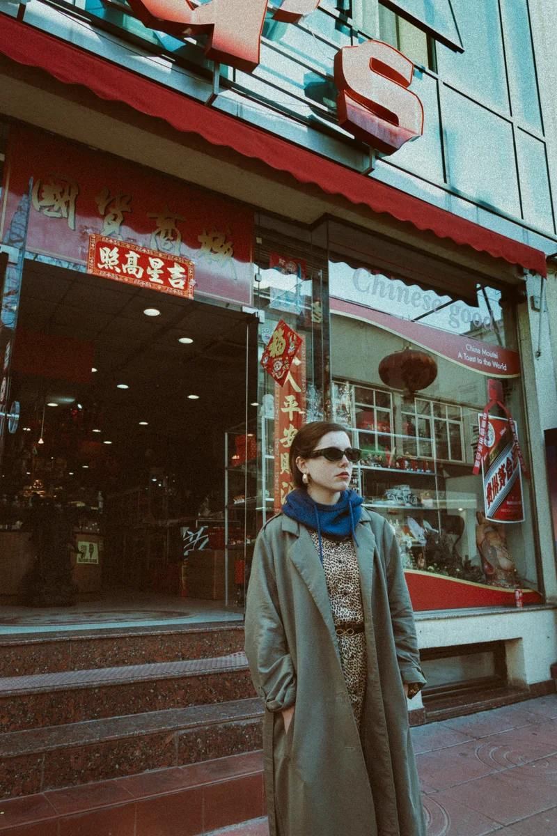 Woman in a grey trench coat and sunglasses outside a Chinese shop