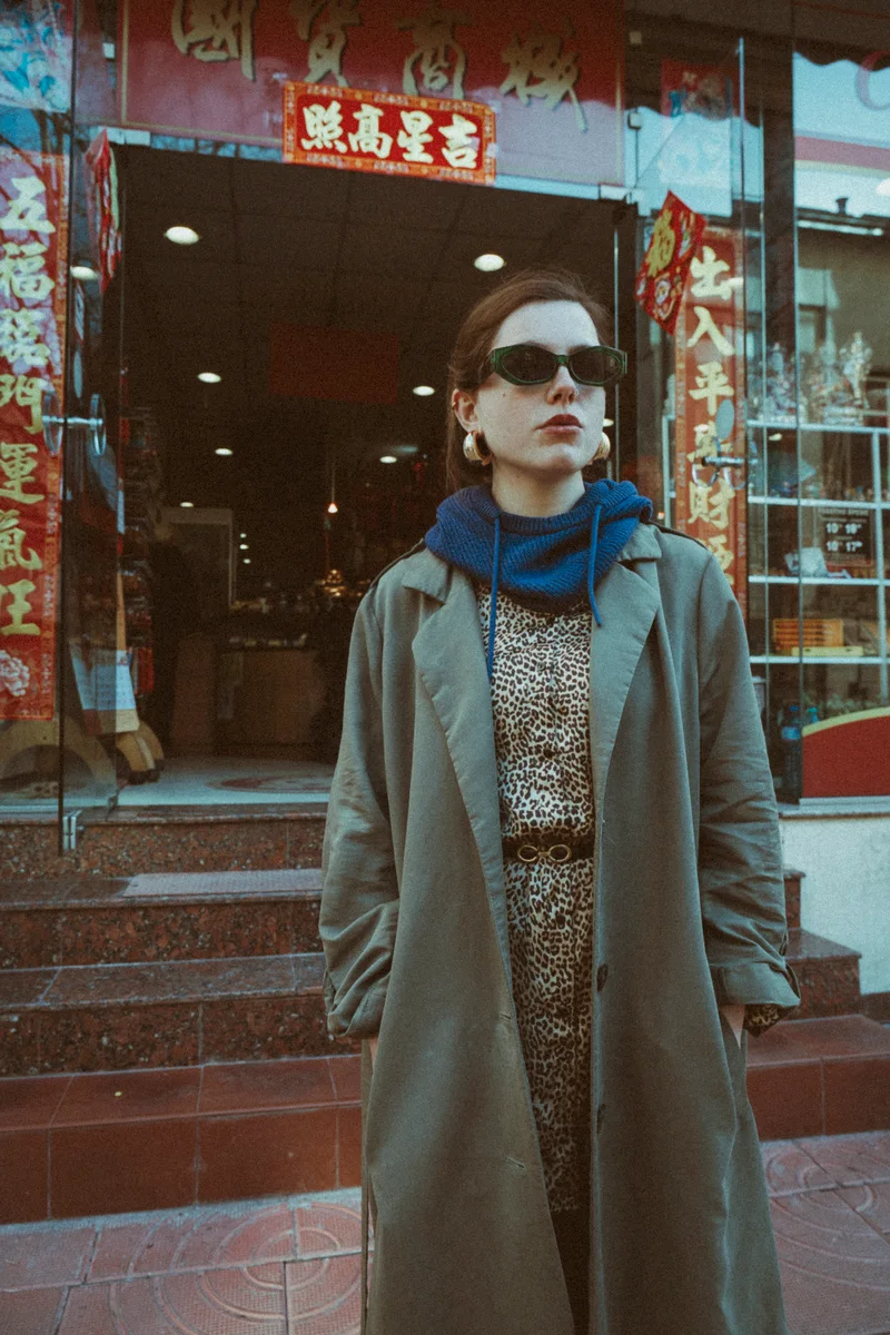 Woman in a trench coat and a leopard-print dress outside a shop with red signs