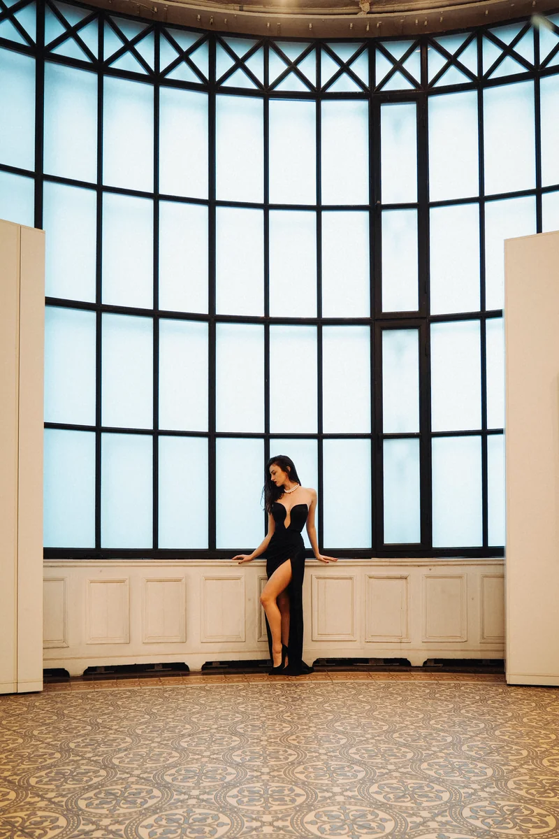Woman in a black evening gown before a vast window in a hall with a patterned floor