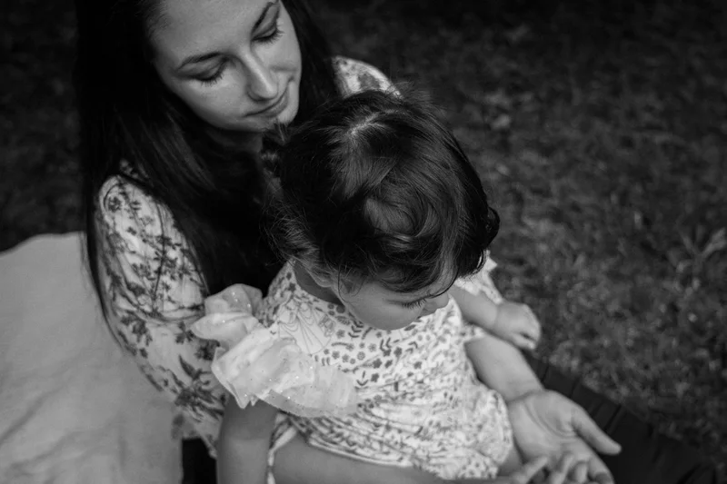 Woman with a child on her lap, both looking down, in black and white