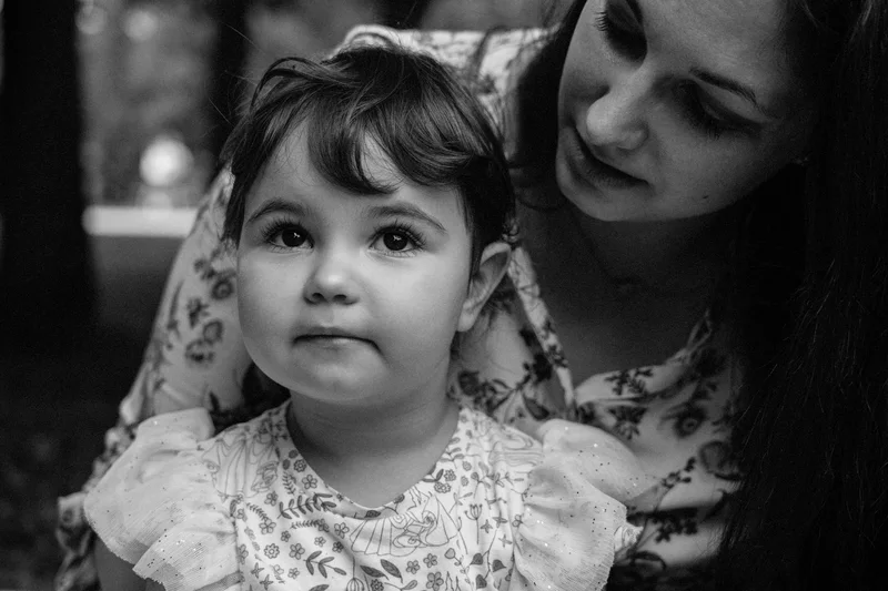 Small child in a ruffled dress, a woman behind gazing at the child, in black and white
