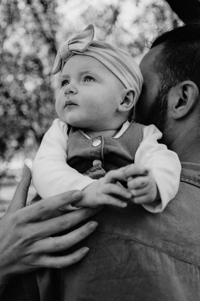 Baby with a bow on a man's shoulder looking up, in black and white