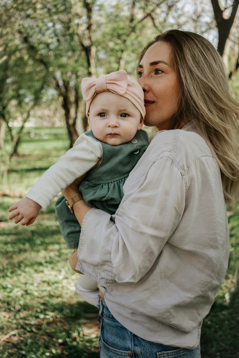 Woman with long blonde hair holding a baby with a pink bow in the park