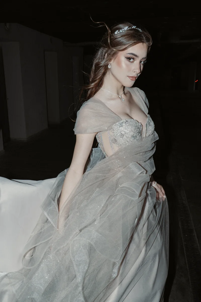 Woman in a pale tulle dress looking aside against a dark garage backdrop
