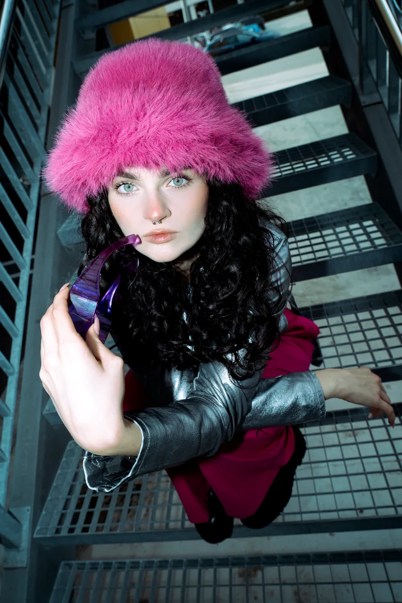 Woman in a bright pink hat looking up from a metal staircase