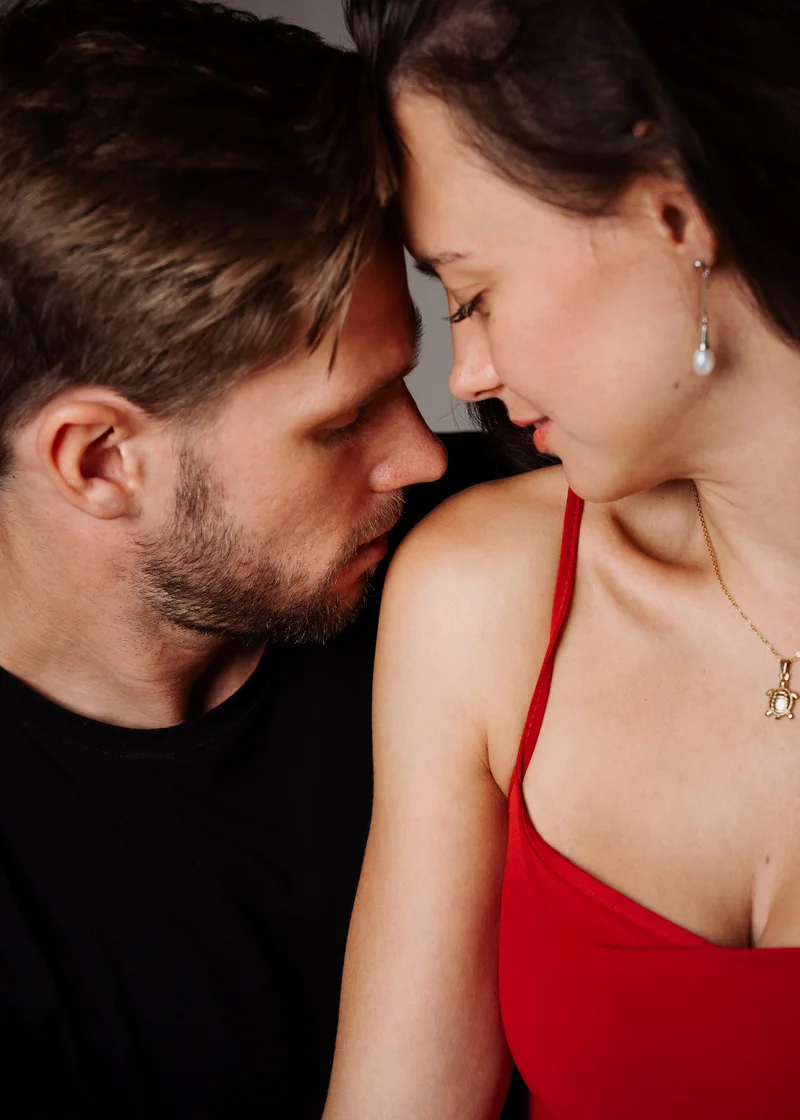 Bearded man and a woman in red touching faces in warm close light