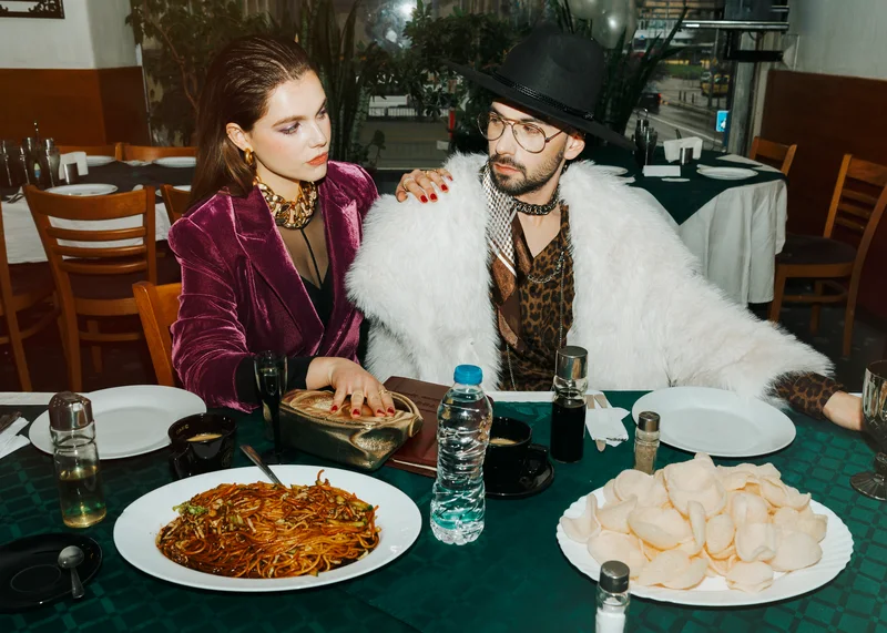 Couple in vintage clothes sitting beside plates of food in a small restaurant