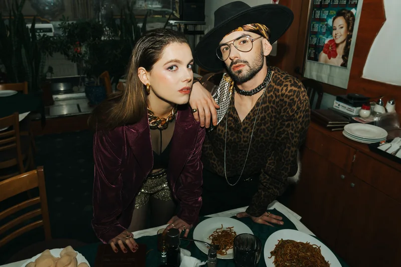 Couple in burgundy and a fur coat looking aside from a restaurant table