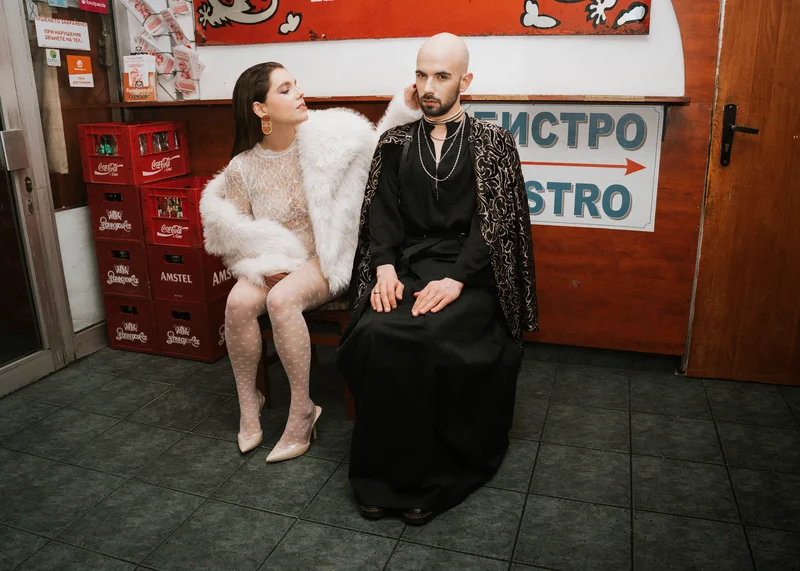 Woman in white and a man in a fur coat sitting on chairs outside a bistro