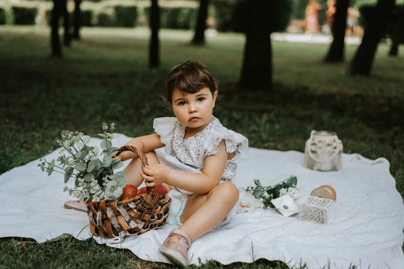 Small child sitting on a white blanket on the grass, looking at the camera