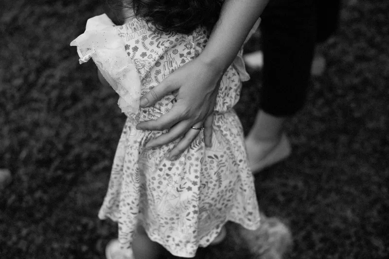 Adult hand on the back of a child in a floral dress, in black and white