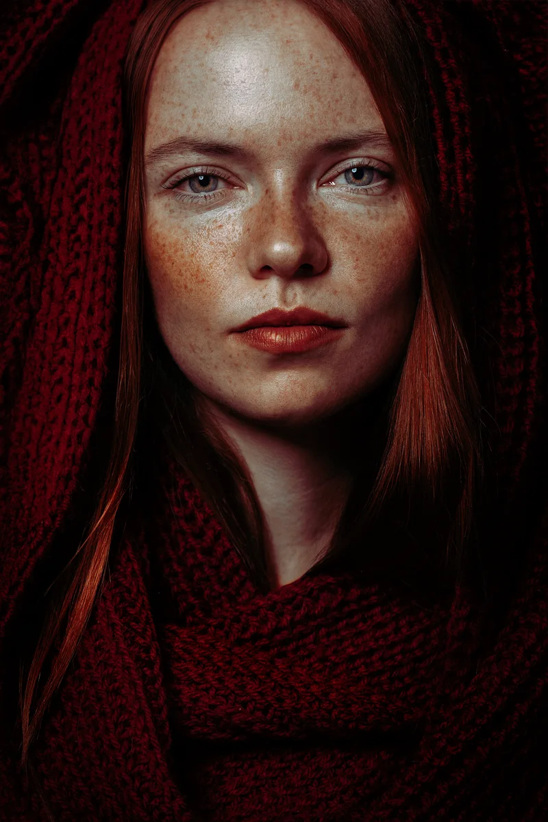 Freckled woman with red hair wrapped in a chunky burgundy knit scarf