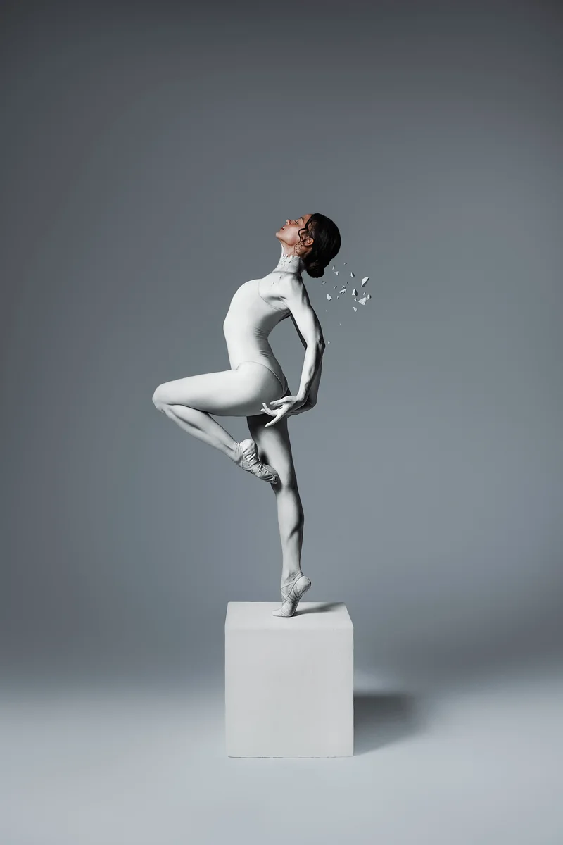 Dancer in a white bodysuit balancing on tiptoe on a white plinth