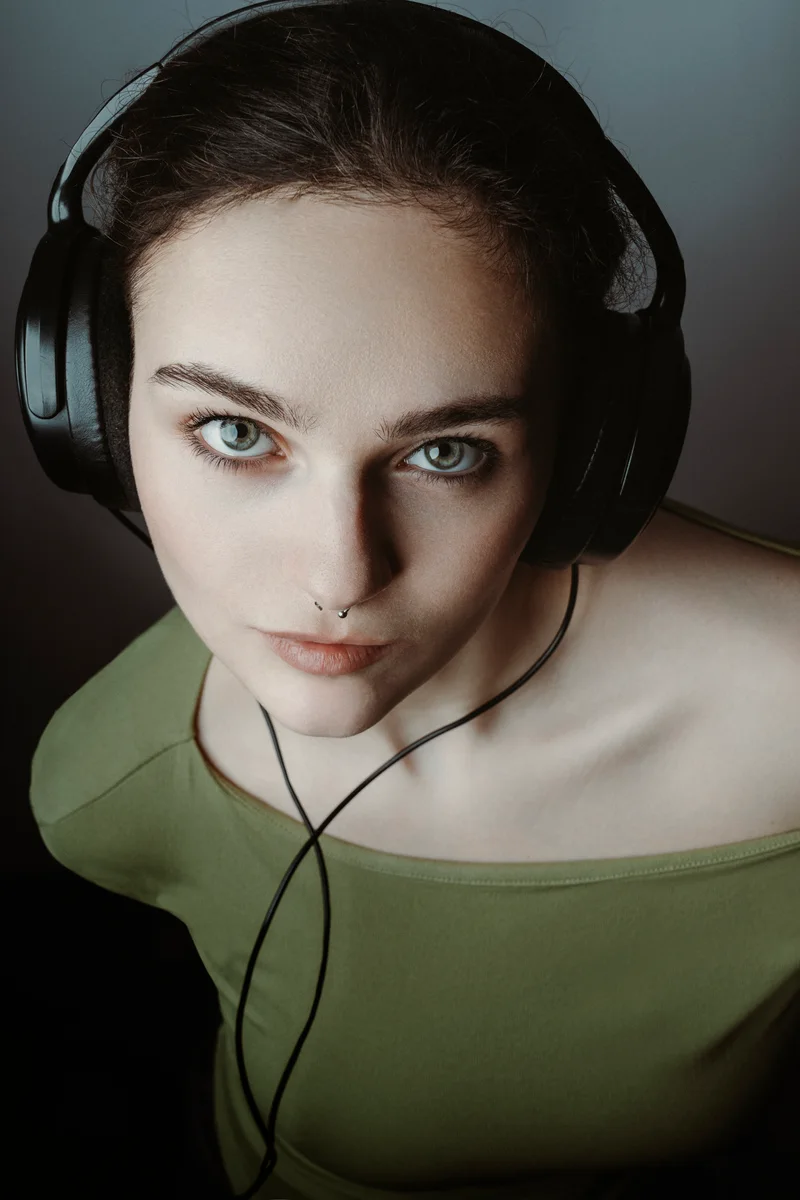 Woman wearing headphones and a green top looking up at the camera