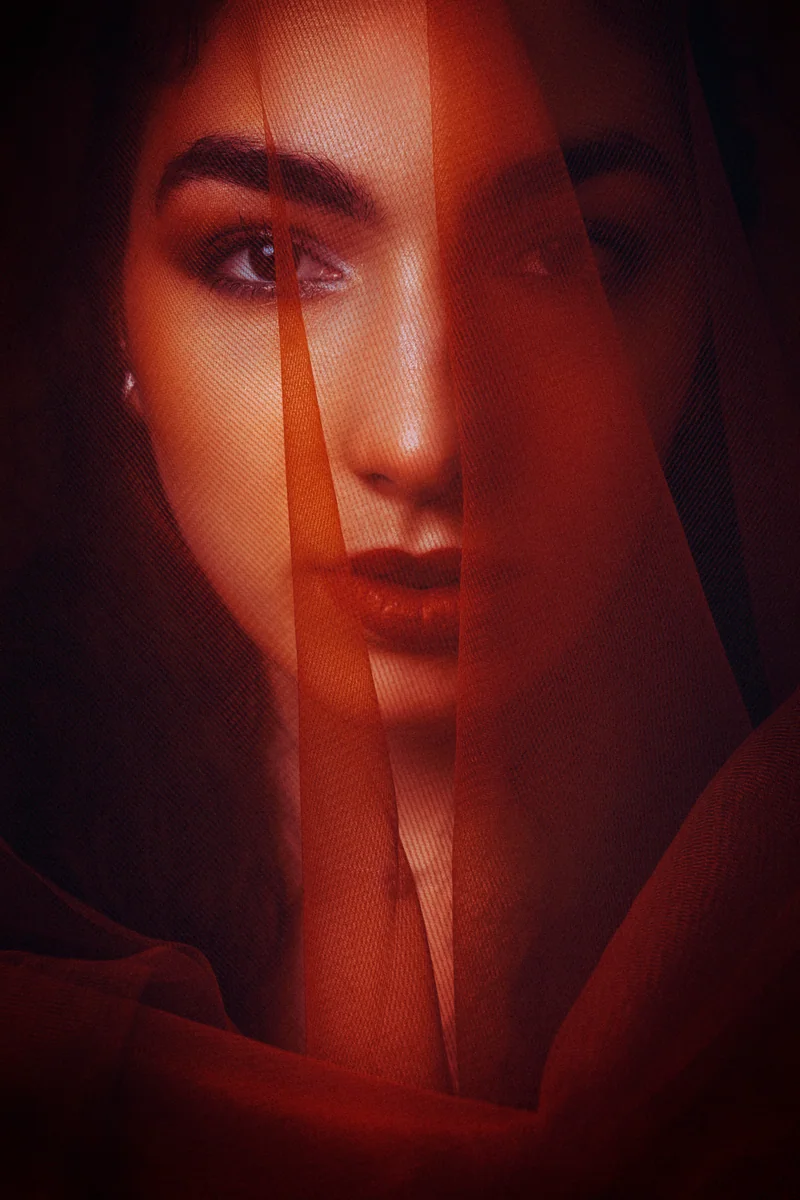 Woman's face behind a sheer red veil in orange light