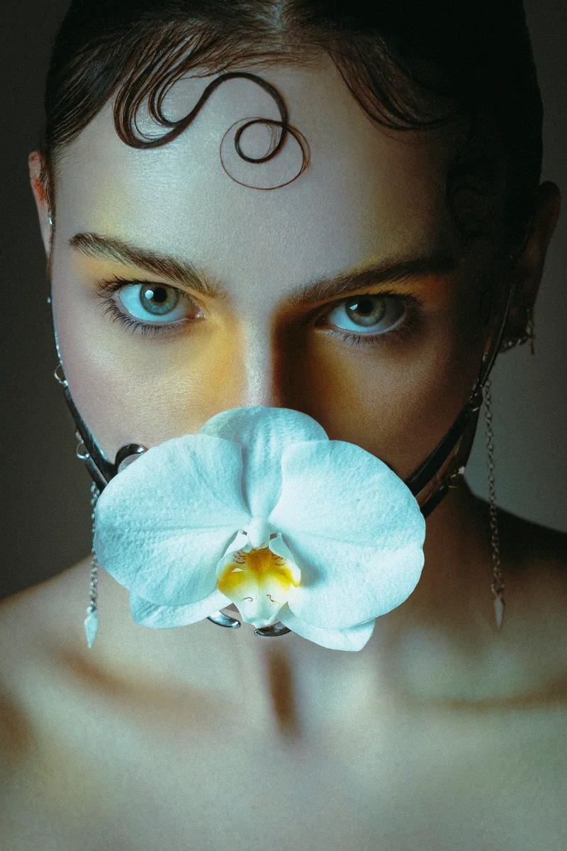 Woman with a white orchid over her mouth and a curl on her forehead