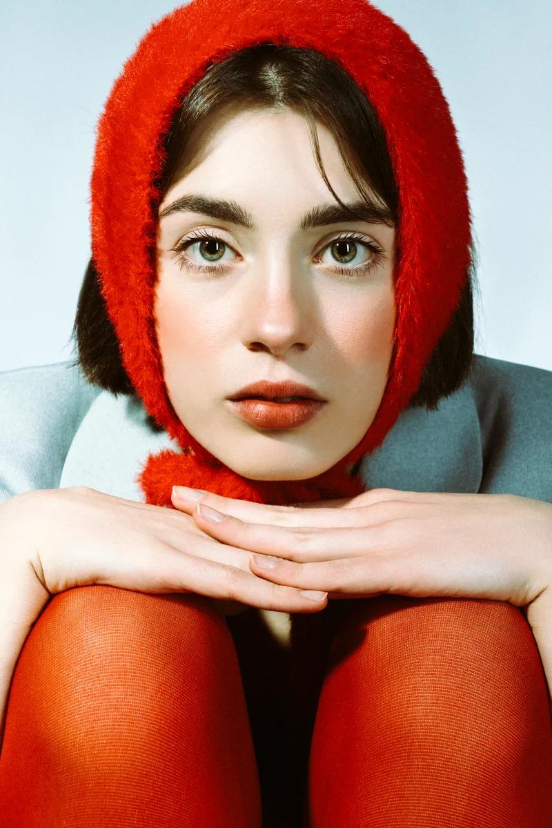 Woman in a red bonnet resting her chin on her hands on her knees