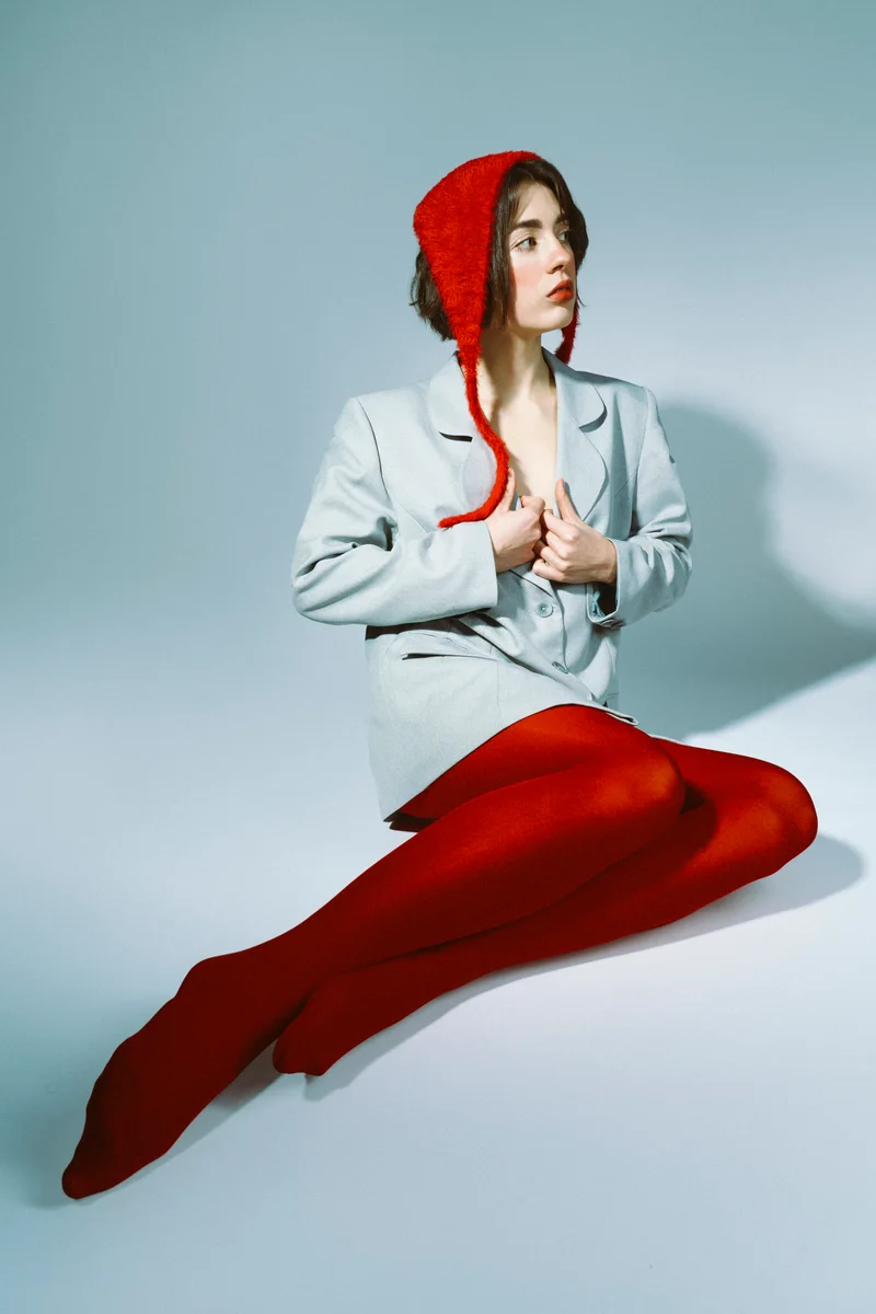 Seated woman in a red bonnet, grey blazer and red tights