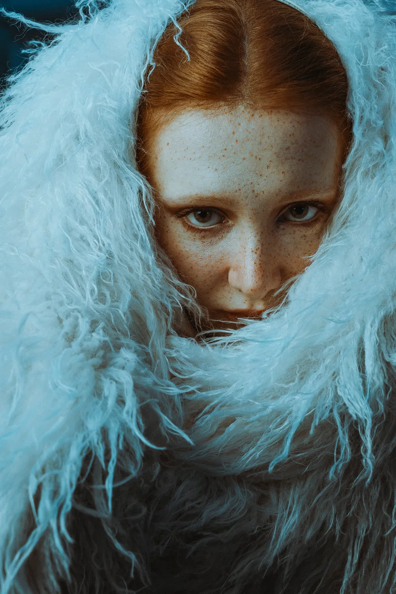 Freckled woman looking towards the camera from beneath pale blue feathers
