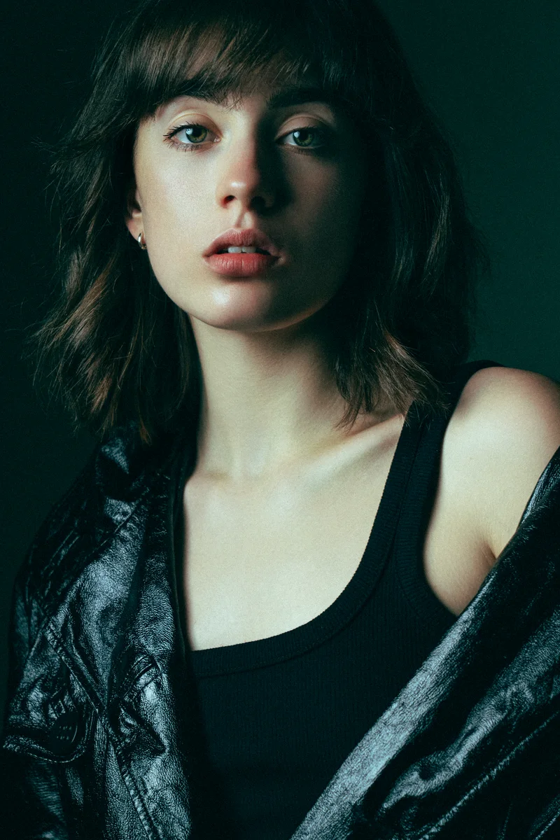 Woman with a fringe in a black top, a leather jacket slipping off her shoulder