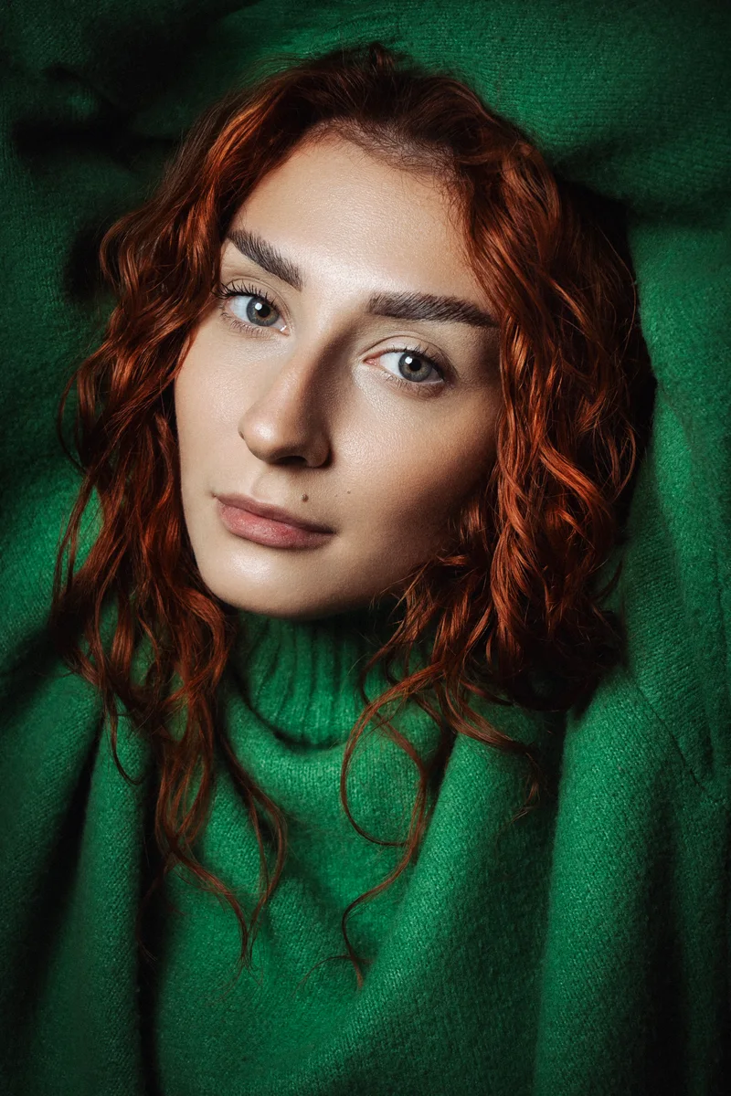 Red-haired woman in a green sweater leaning forward in soft shadows