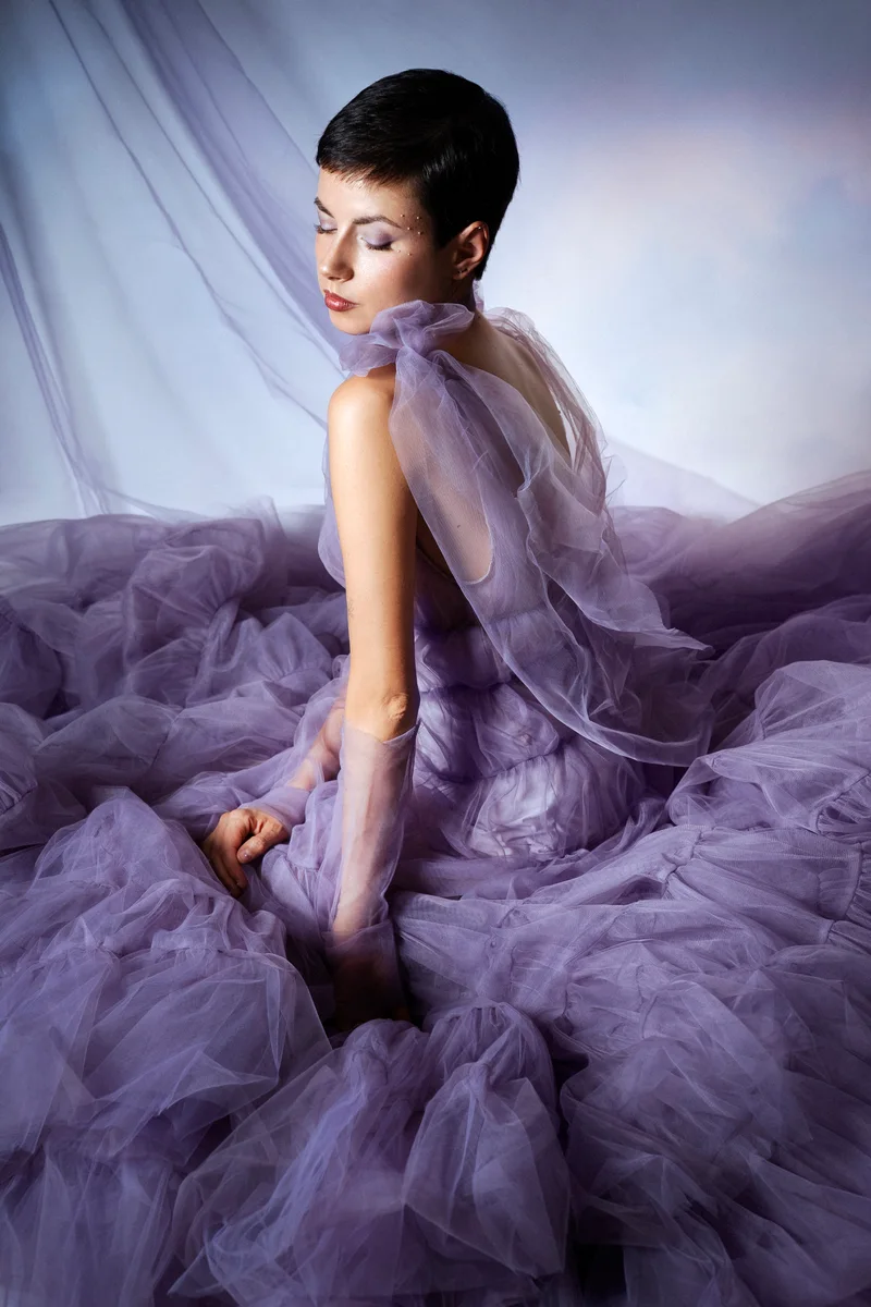Woman with short hair sitting in purple tulle and looking over her shoulder