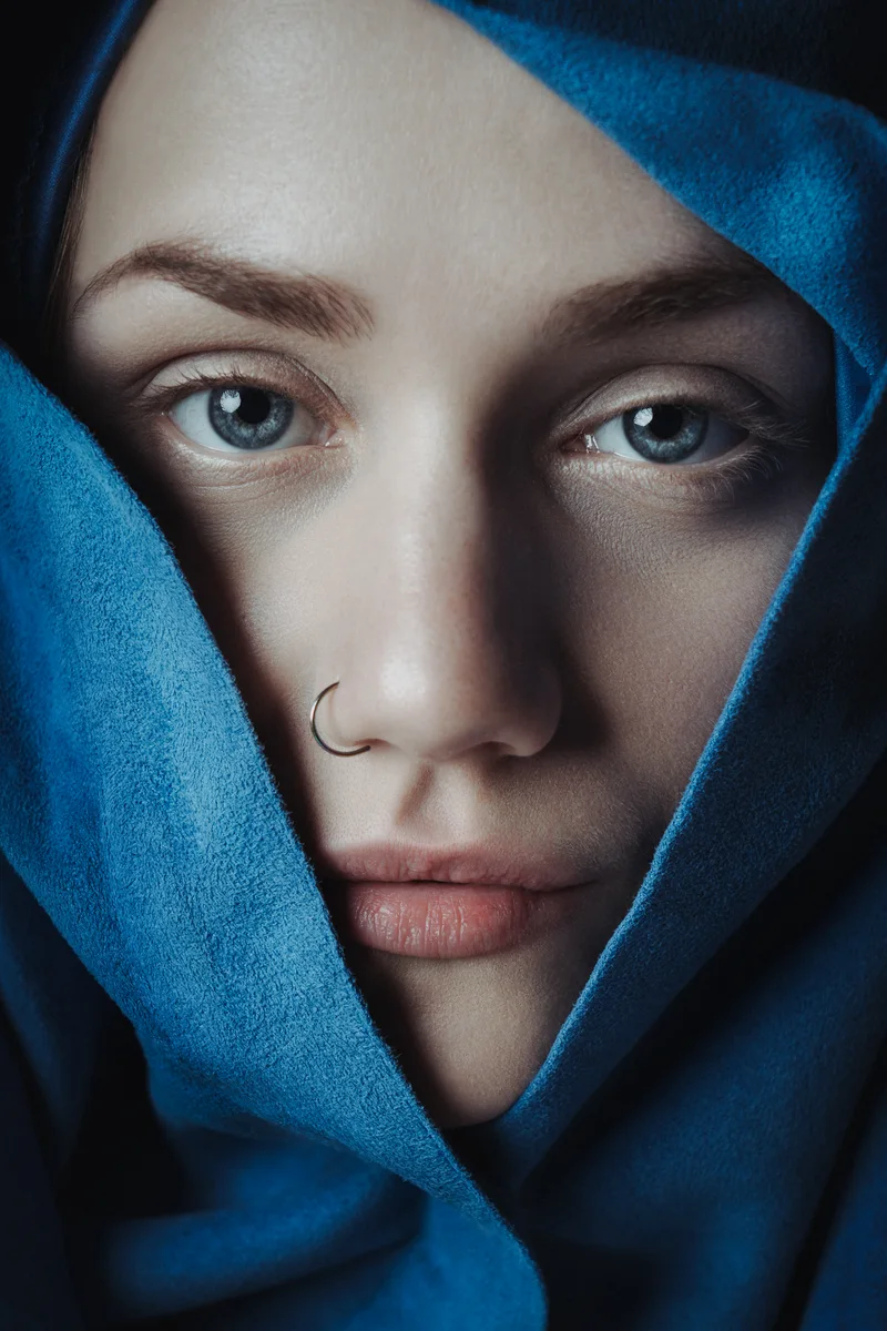 Woman's face with a nose ring, framed by a blue cloth