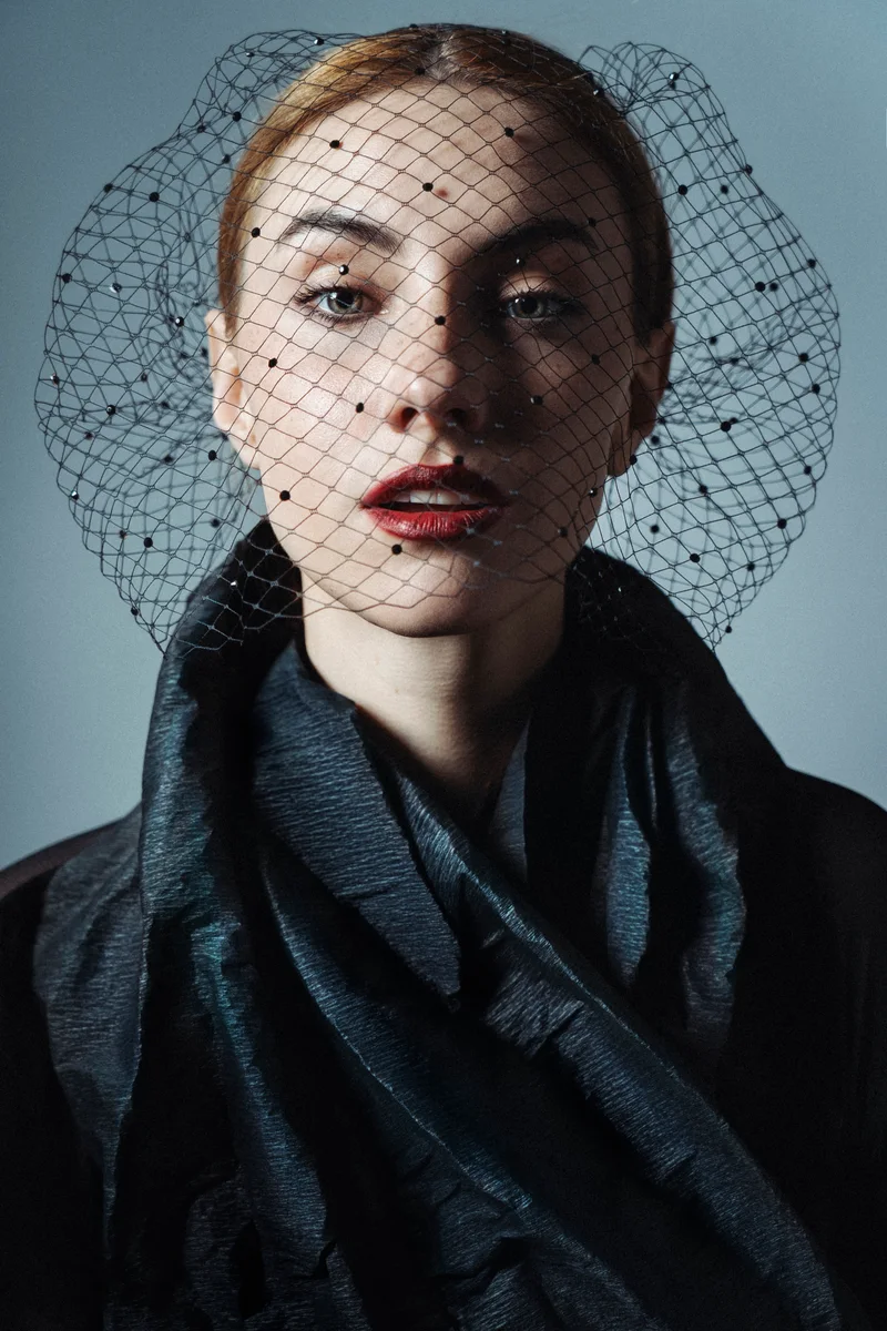Woman with swept-back hair, a round net veil and dark drapery