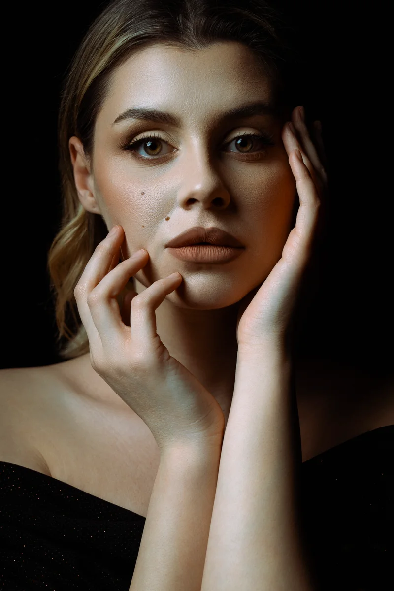 Blonde woman with her hands framing her face against black