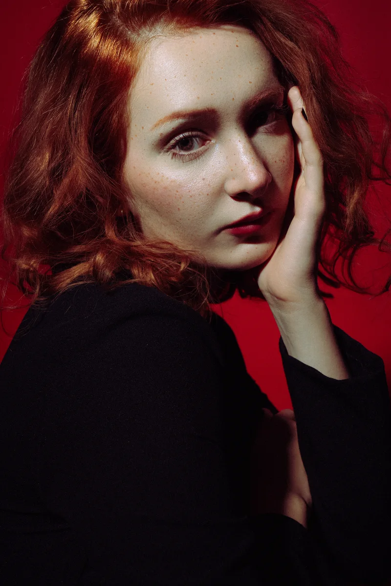 Red-haired woman touching her face against a deep red backdrop
