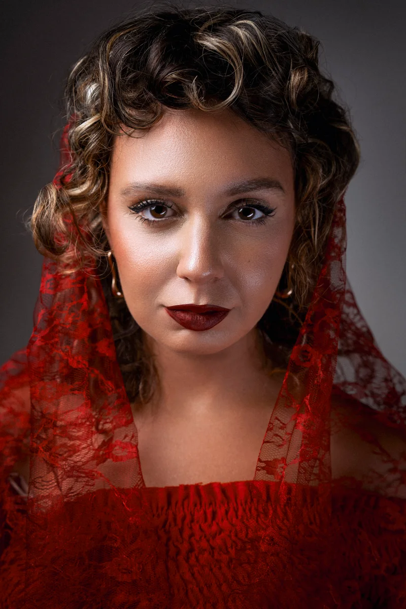 Woman with curls, red lace and a knitted scarf looking straight ahead