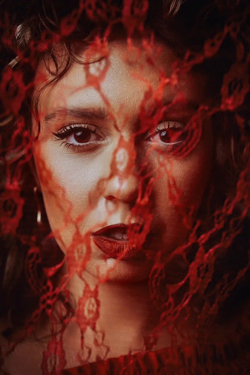 A curly-haired woman's face framed by transparent red lace
