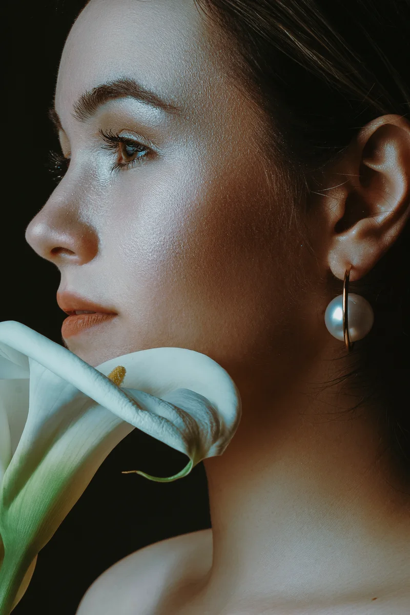Woman in side profile with a pearl earring and a white calla lily beside her chin