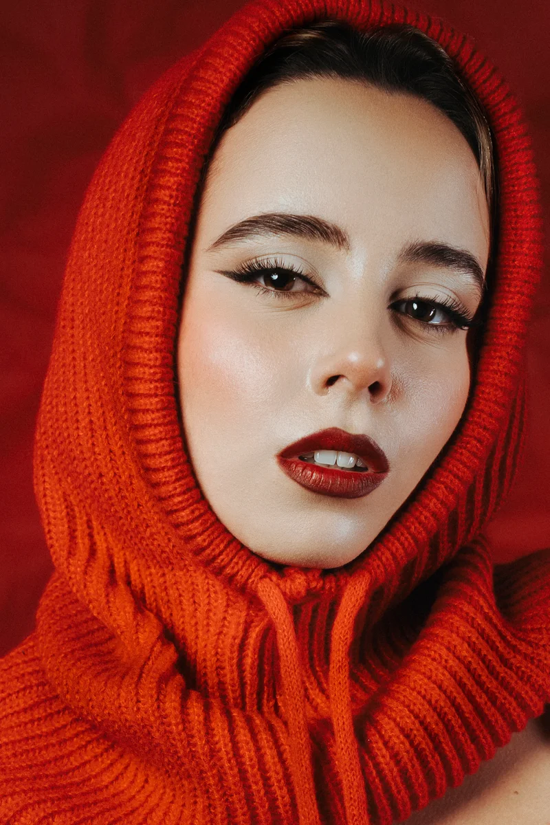 Woman in a red knitted hood with dark red lipstick against red
