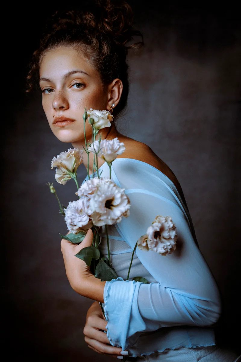 Woman in a sheer pale blue top holding white flowers to her chest