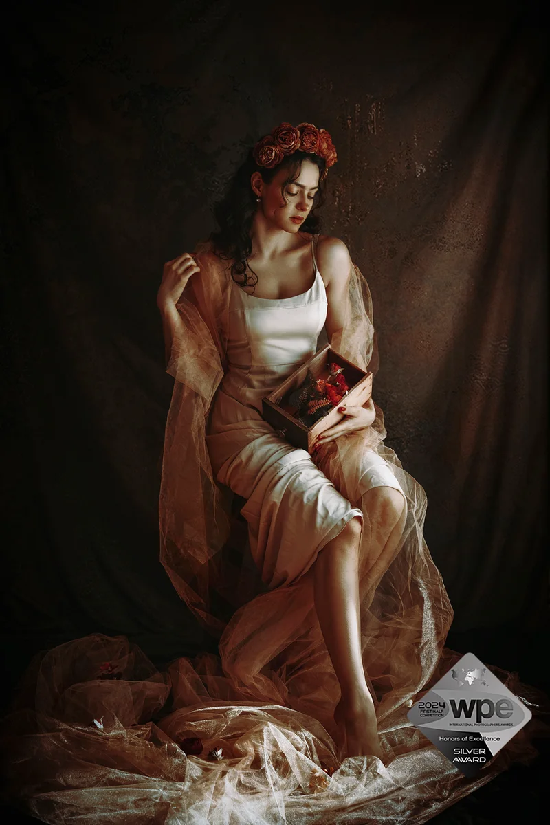 Seated woman with flowers in her hair and a pale dress amid brown drapery