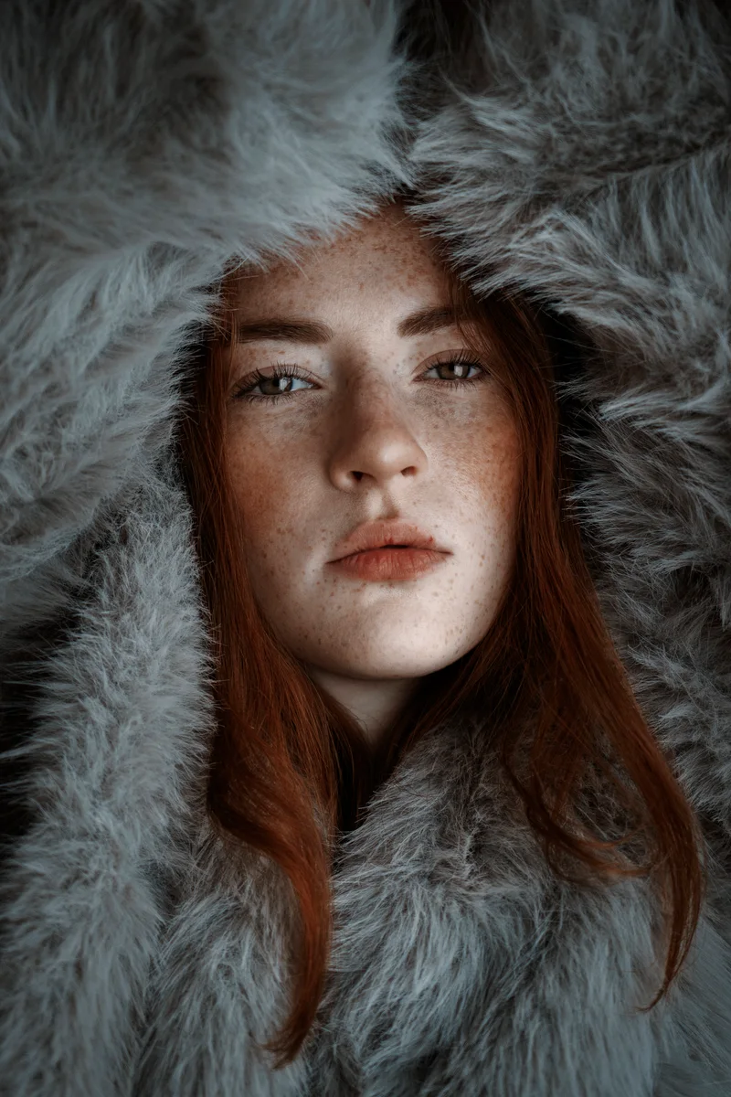 Freckled red-haired woman in a hood of grey fur