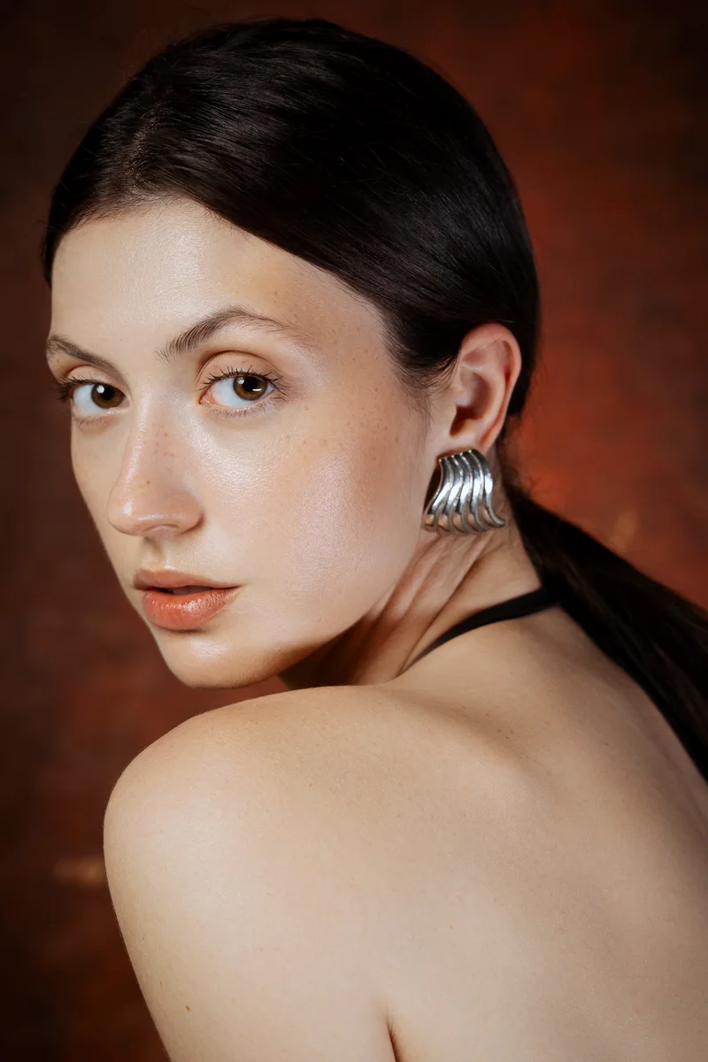 Woman with slicked-back dark hair and a large silver earring looking over her bare shoulder