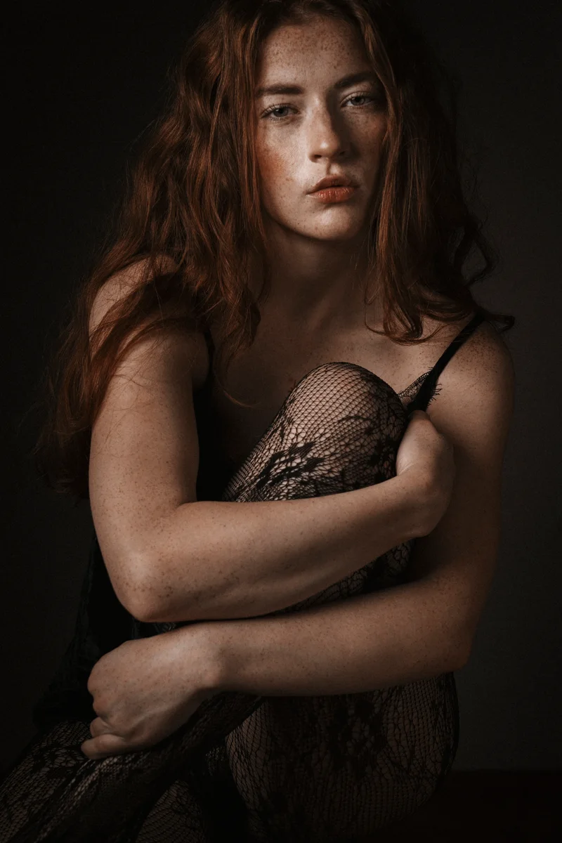Red-haired woman in black lace sitting with her arms around her knees