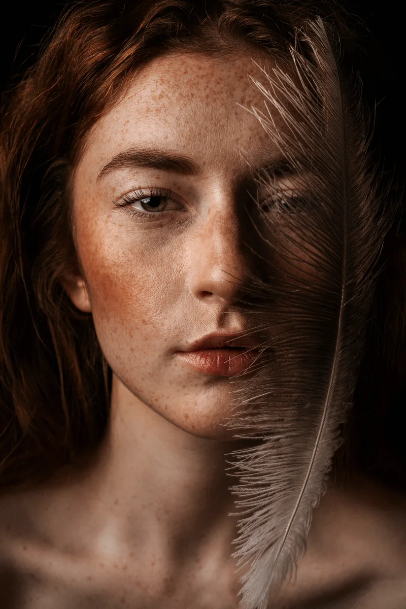 Freckled woman with a white feather across half of her face