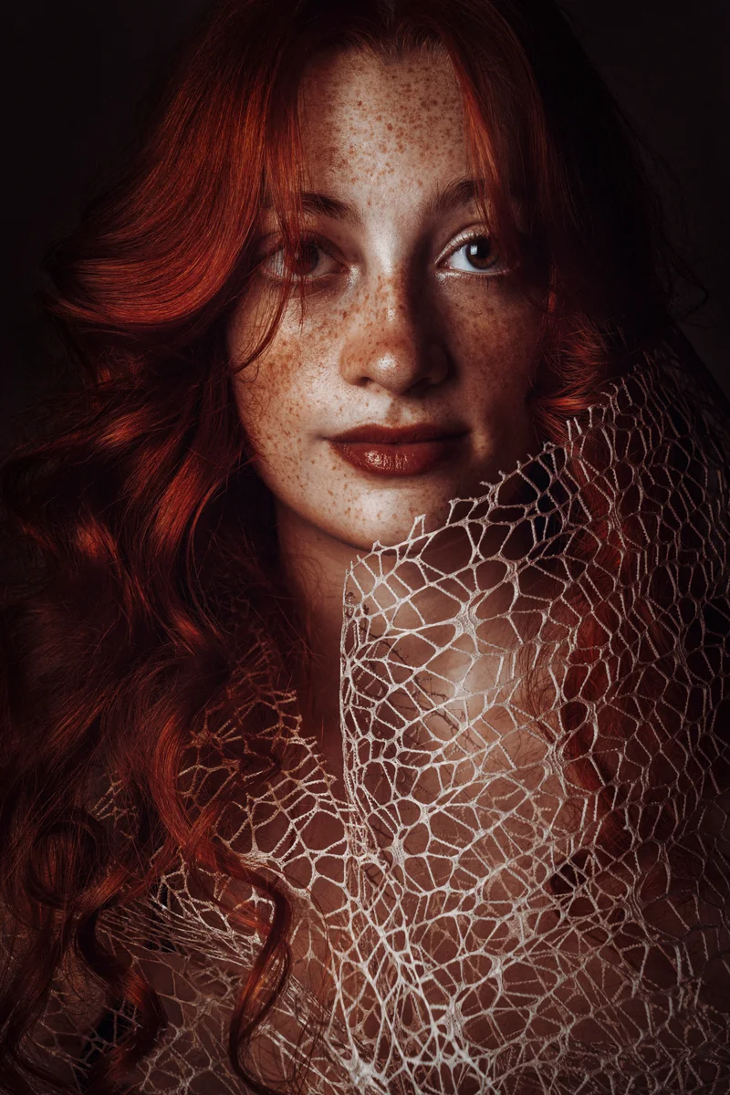 Freckled red-haired woman behind a white web-like mesh