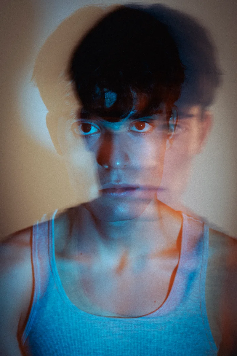 Portrait with overlapping faces in blue light and a grey vest