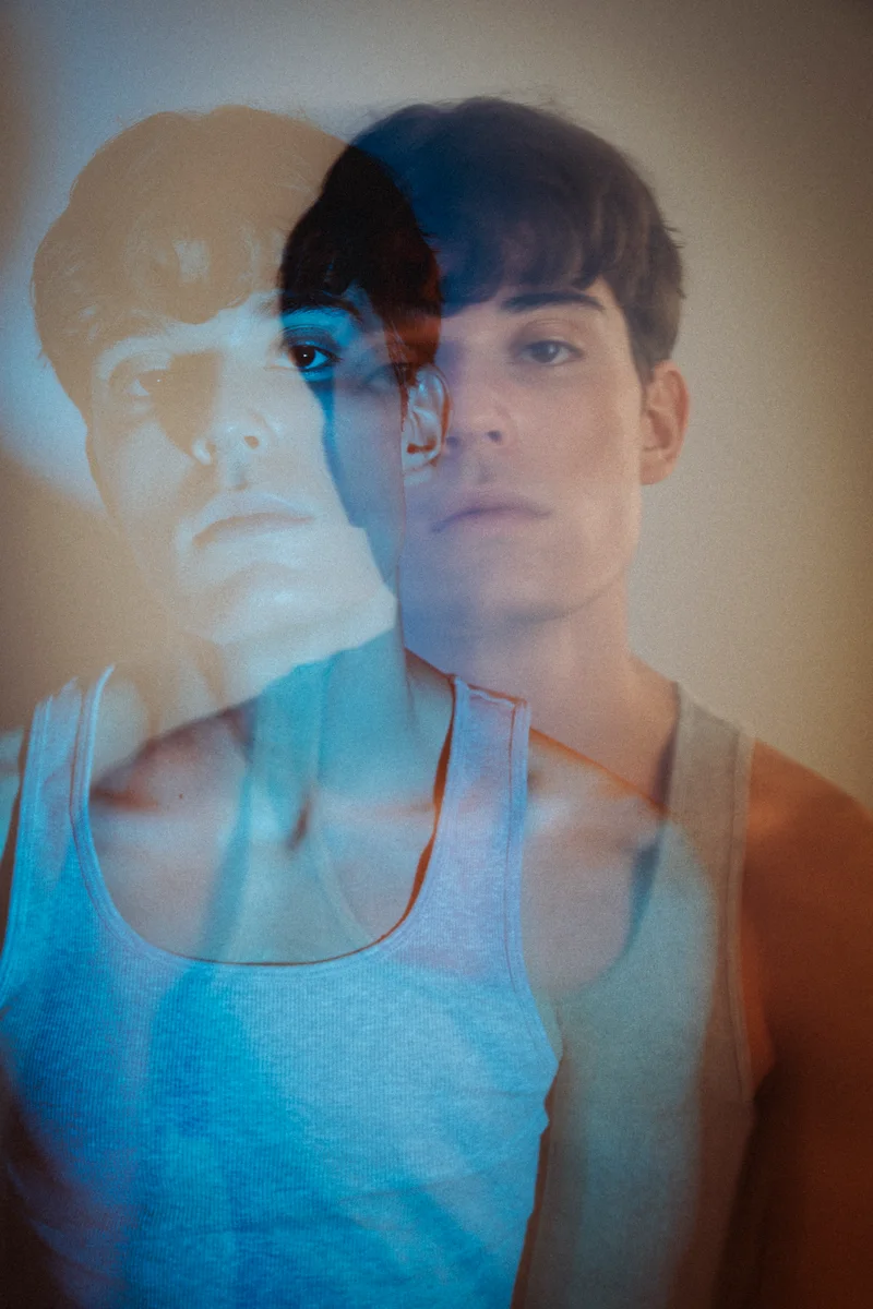 Double exposure of a face in blue and warm light against a pale backdrop